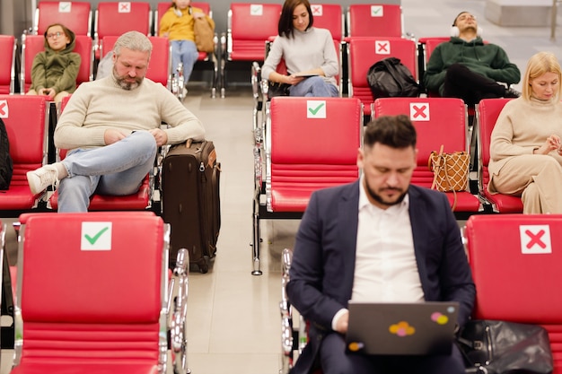 Personas sentadas en sillas en la sala de espera del aeropuerto y esperando su salida