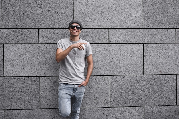 Personas, tecnología, viajes y turismo: hombre con auriculares, teléfono inteligente en la calle de la ciudad y escuchando música sobre fondo de pared gris