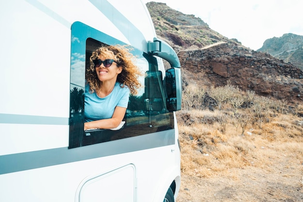 Foto personas y viajes destino de vacaciones feliz mujer adulta joven sonríe y disfruta de la naturaleza fuera de la carretera de estacionamiento fuera de la ventana de su moderna casa rodante autocaravana mujer viajera