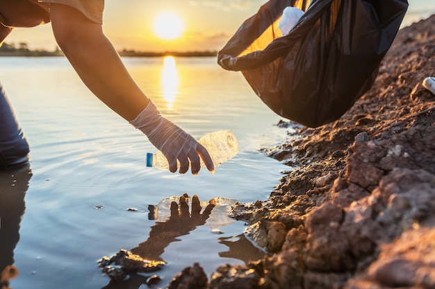 Personas voluntarias manteniendo la botella de plástico de basura en una bolsa negra en el río al atardecer