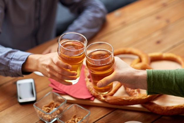 Personen-, Freizeit- und Getränkekonzept - Nahaufnahme männlicher Hände, die Biergläser und Brezeln auf dem Tisch in der Bar oder Kneipe klirren