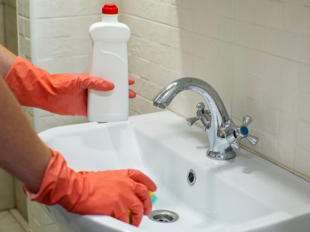 Personenhand, die ein Reinigungsmittel in einer weißen Flasche hält, um das Waschbecken zu reinigen