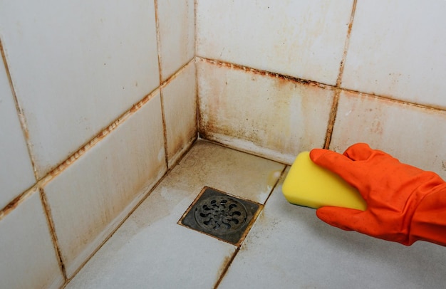 Personenhand, die einen gelben Schwamm hält und ein schmutziges Waschbecken in Rost reinigt, schmutzige Waschbecken reinigen.