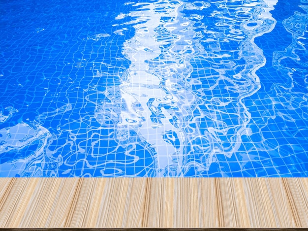 Foto perspectiva de la mesa de madera, olas de agua azul en la piscina y reflejos del hotel.