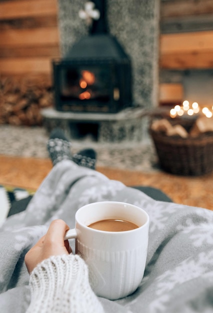 Foto perspectiva personal de una mujer con un suéter cálido sosteniendo una taza de café frente a la chimenea