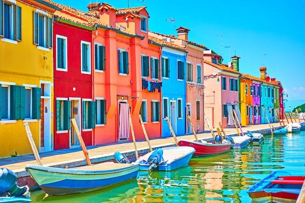 Perspektive des Kanals mit Booten und malerischen Häusern in Burano am sonnigen Sommertag, Venedig, Italien