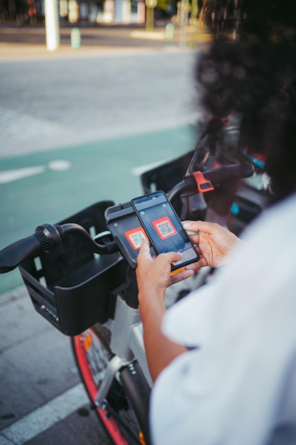 Perspektivische Aufnahme einer Frau, die einen QR-Code mit dem Telefon scannt, um ein Elektrofahrrad in der Stadt zu mieten