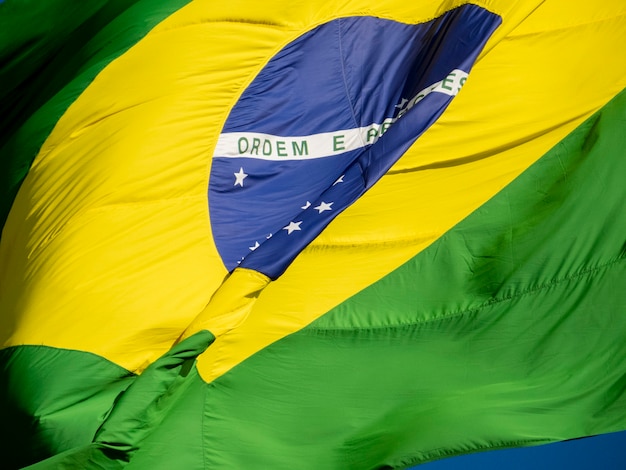 Foto perto da bandeira brasileira tremulando ao vento. no centro da bandeira com as palavras 