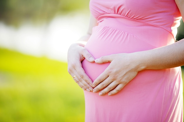 Perto da barriga de grávida, as mãos formando um coração acima do bebê. futura mãe esperando bebê. conceito de maternidade. copie o espaço para mensagem de texto