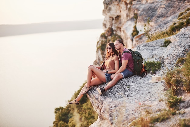 Foto perto da borda. jovem casal descansando de uma caminhada à beira da montanha. quer saber a que distância fica a outra costa.