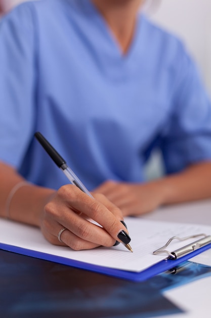 Perto da enfermeira, escrevendo o diagnóstico do paciente na área de transferência no escritório do hospital. médico de saúde usando o computador na clínica moderna, olhando para o monitor, medicina, profissão, esfrega.