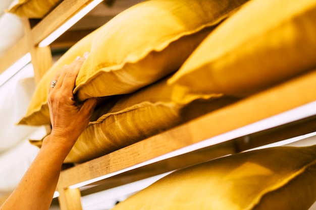 Foto perto da mão de uma mulher caucasiana, escolha e pegue o travesseiro amarelo de uma loja de decoração para casa em um centro comercial - compras e estilo de vida de pessoas