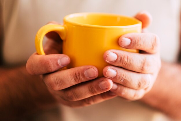 Perto da mão de uma mulher pegando uma grande xícara amarela de bebida quente como chá ou café