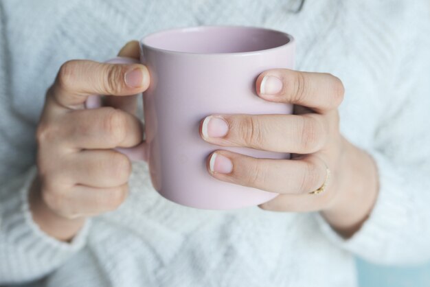 Foto perto da mão de uma mulher segurando a xícara de café de cor rosa.
