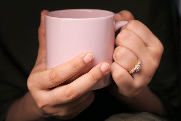 Perto da mão de uma mulher segurando a xícara de café de cor rosa.