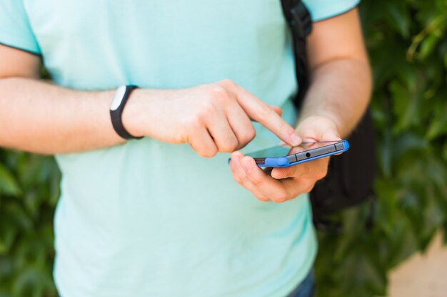 Perto da mão masculina com um rastreador de fitness e telefone inteligente ao ar livre.