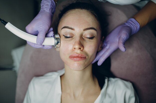 Perto da mulher chefe recebendo terapia facial de fonoforese de eletroporação no salão de beleza do spa.