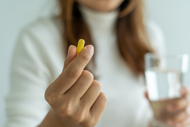 Perto da mulher da mão segurando um suplemento dietético, medicamento ou vitamina e um copo de água pronto para tomar. conceito de saúde, medicina, autocuidado, doença e farmácia.