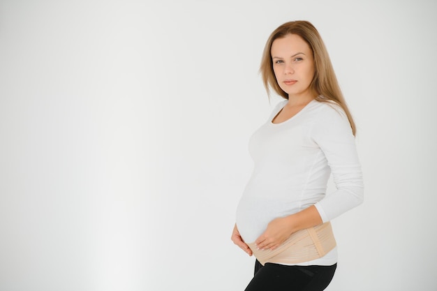 Perto da mulher grávida colocando uma bandagem no fundo cinza com espaço de cópia. Conceito de cinto de suporte abdominal ortopédico.