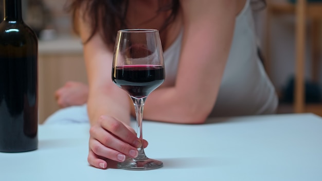 Perto da mulher segurando uma taça de vinho tinto na mesa. pessoa infeliz que sofre de enxaqueca, depressão, doença e ansiedade, sentindo-se exausta com sintomas de tontura e com problemas de alcoolismo.