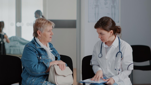 Perto da mulher sênior e médico falando sobre diagnóstico na sala de espera, dando conselhos médicos e suporte ao paciente doente. Pensionista discutindo com o médico sobre saúde no saguão.