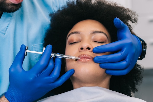 Perto das mãos da especialista em esteticista, injetando botox nos lábios femininos.