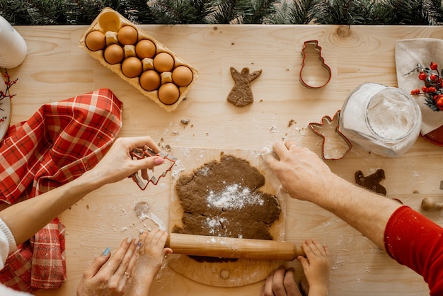 Foto perto das mãos da jovem família, prepare biscoitos de natal em uma mesa de madeira com muitos ingredientes para cozinhar.
