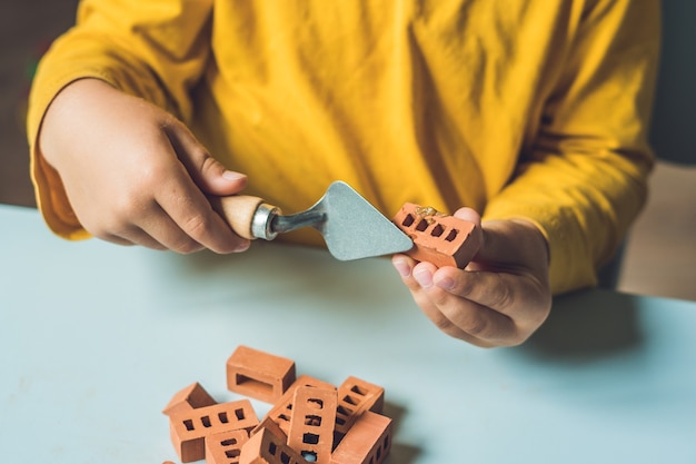 Foto perto das mãos de uma criança brincando com pequenos tijolos de barro reais na mesa