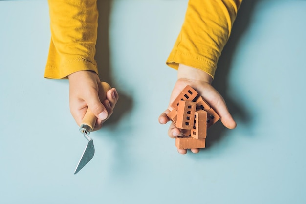 Perto das mãos de uma criança brincando com verdadeiros pequenos tijolos de barro na mesa. criança se divertindo e construindo com tijolos de barro pequenos reais. aprendizagem precoce. desenvolvimento de brinquedos. conceito de construção