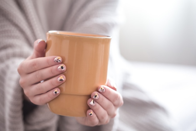 Perto de belas mãos femininas segurando uma xícara grande de cappuccino, café e flores