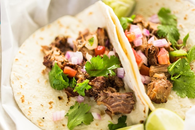 Perto de carnitas de porco desfiada com pico de gallo em uma tortilha de farinha.