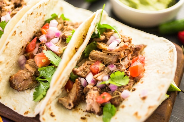 Perto de carnitas de porco desfiada com pico de gallo em uma tortilha de farinha.