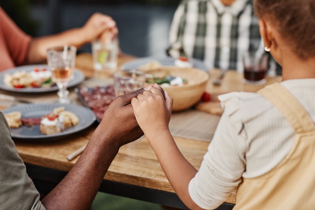 Perto de crianças de mãos dadas em jantar em família ao ar livre e rezando no espaço da cópia