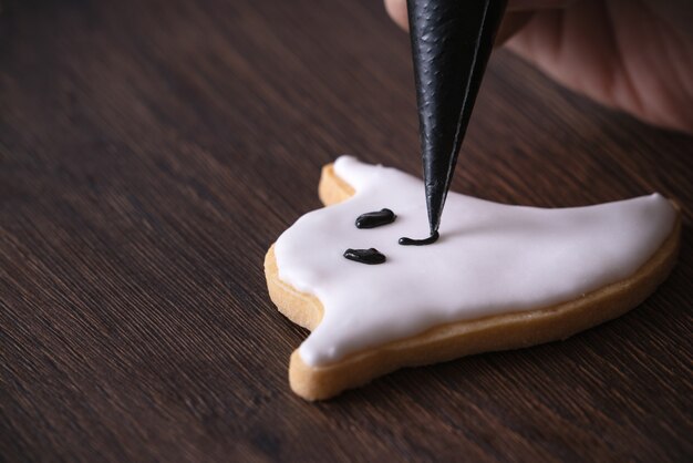 Perto de decorar biscoitos de gengibre fantasma de Halloween fofos com saco de cobertura de creme de confeiteiro de glacê.