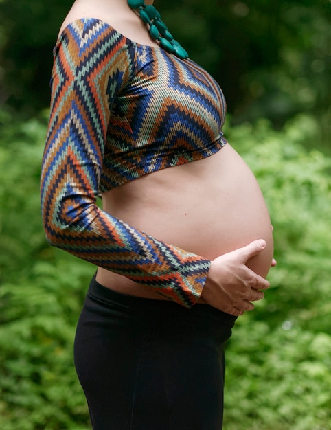 Perto de grávida moderna jovem tocando sua barriga ao ar livre.