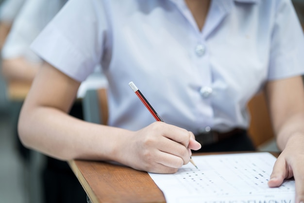 Perto de jovens estudantes universitários, concentre-se em fazer o exame em sala de aula. Aluna escreve no papel de resposta de exames em sala de aula.