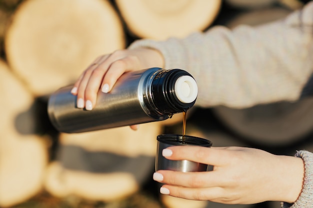 Perto de mãos femininas servindo uma bebida quente em uma caneca térmica