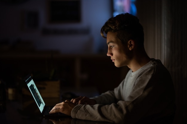 Perto de um adolescente caucasiano trabalhando ou estudando sozinho em casa à noite com seu laptop ou computador - aula online em estilo de vida de bloqueio de conceito de quarentena