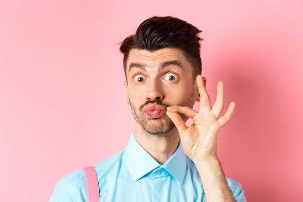 Perto de um cara engraçado caucasiano tocando seu bigode francês, lábios franzidos e parecendo bobo, em pé rosa.