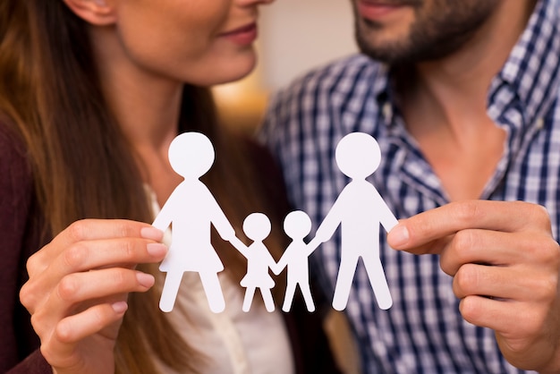 Foto perto de um casal segurando a corrente de homem de papel de uma família. jovem casal decidindo sobre planejamento familiar. close-up da corrente do homem de papel de uma família. mãos do pai segurando uma família de papel.