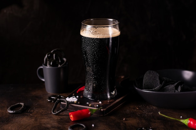 Foto perto de um copo grande de cerveja escura, cerveja preta forte em um fundo preto com petiscos