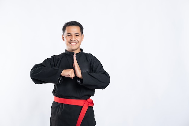 Perto de um homem asiático sorridente usando o uniforme pencak silat e fazendo gestos respeitosos com as mãos