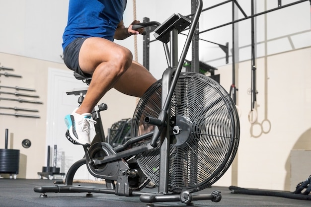 Perto de um homem irreconhecível, fazendo treinamento cardiovascular na máquina de bicicleta estacionária com ventilador em t.