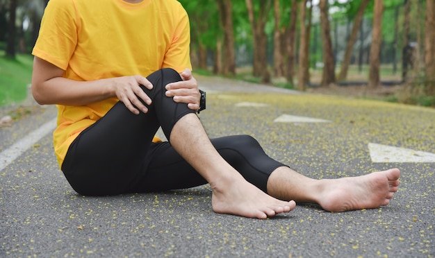 Perto de um jovem esportista asiático com dor nos músculos e articulações durante exercícios ao ar livre, durante o treinamento ou corrida e conceito de lesão esportiva