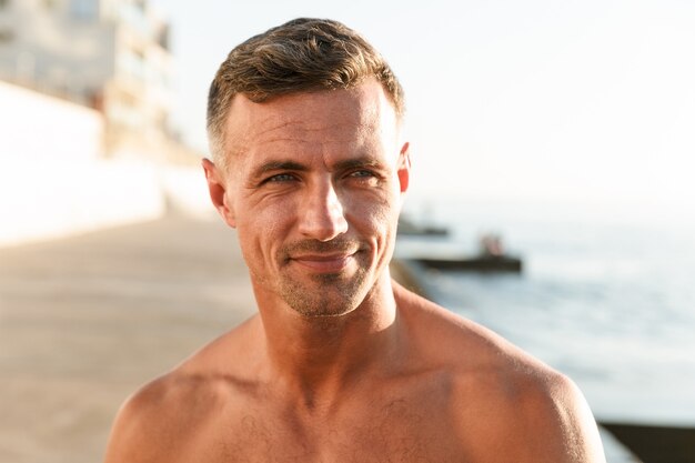 Perto de um sorridente desportista sem camisa na praia