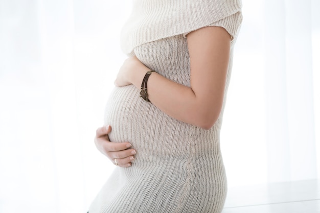 Perto de uma barriga de grávida bonita no fundo da janela. Conceito de estilo de vida de gravidez feliz