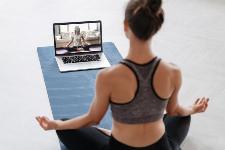 Foto perto de uma jovem mulher desportiva praticando ioga online com o laptop em casa