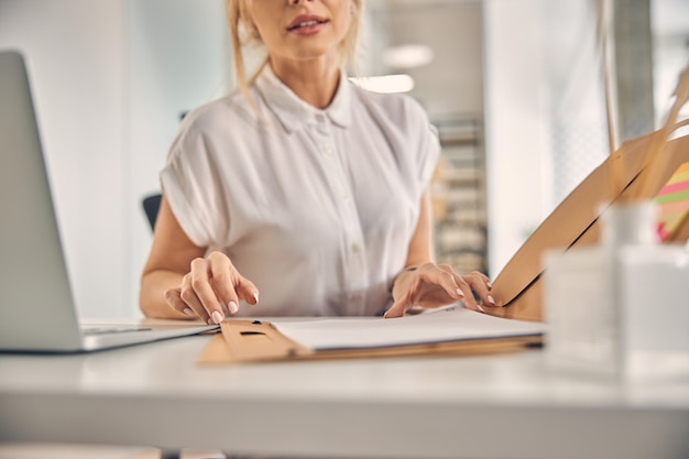 Perto de uma mulher de negócios sentada à mesa com o laptop e verificando a pasta com papéis