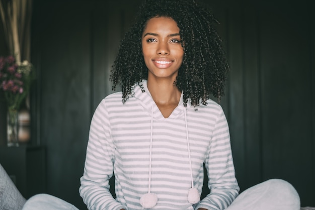 Perto de uma mulher negra com cabelos cacheados, sorrindo e deitada na cama, olhando para longe