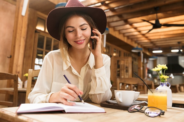 Perto de uma mulher sorridente com chapéu, sentada à mesa do café